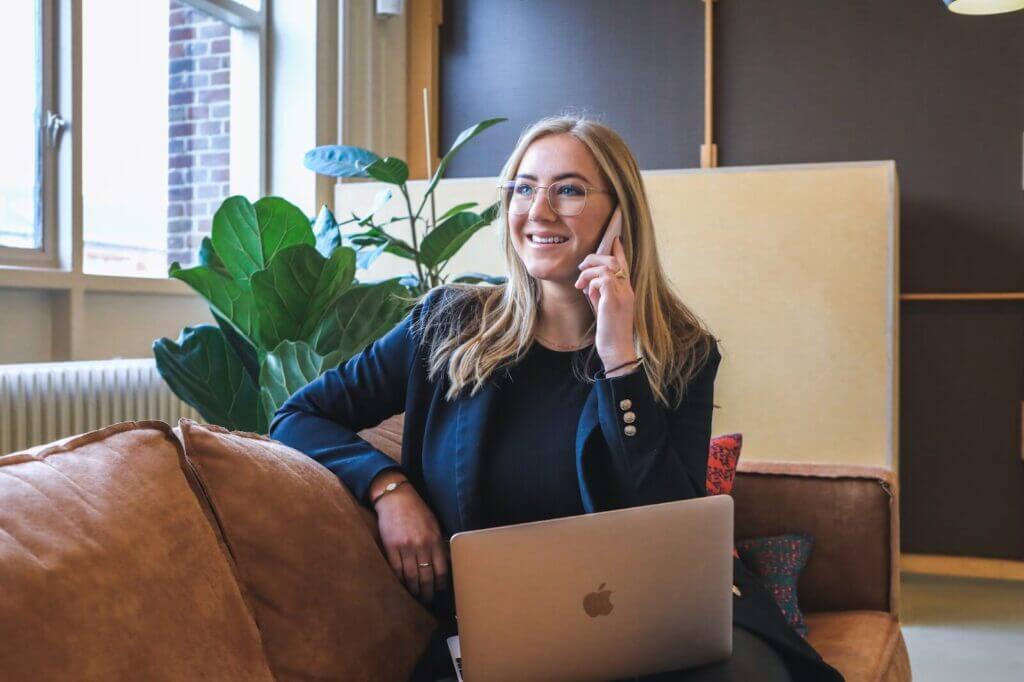 Woman talking on phone with computer in lap running sales outreach